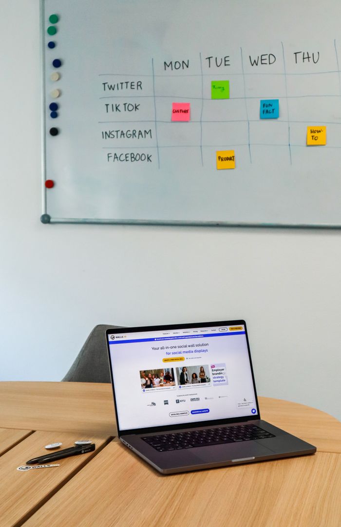 A contemporary office arrangement with a laptop and a whiteboard content calendar for social media platforms.